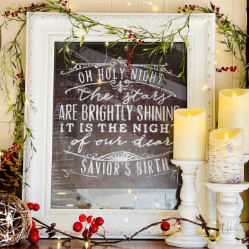 Mantle decorated for Christmas with framed words to a Christmas song, lit candles, greens and twinkle lights.