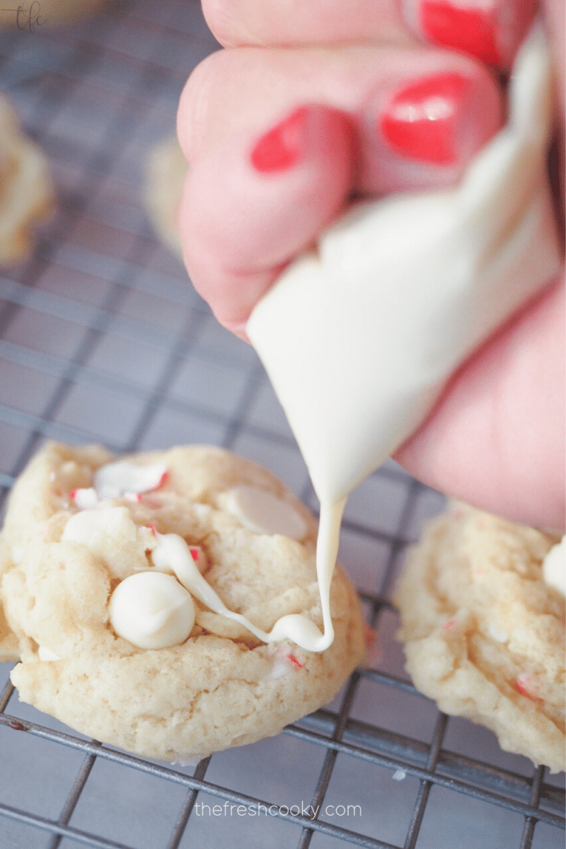 Hand drizzling white chocolate onto peppermint candy cookies. 