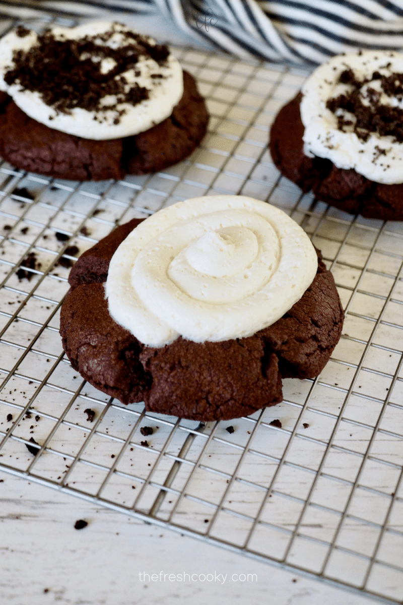 Chocolate Oreo Crumbl Cookie with frosting swirled on top and two finished cookies in background. 