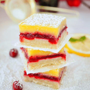 Stacked layered Lemon Cranberry Bars with lemon and powdered sugar dusted on top.