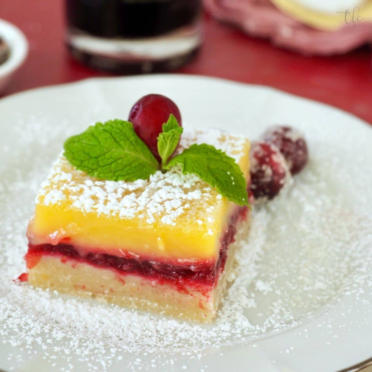 Lemon Cranberry Bars square on plate dusted with powdered sugar and decorated with sugared cranberries.