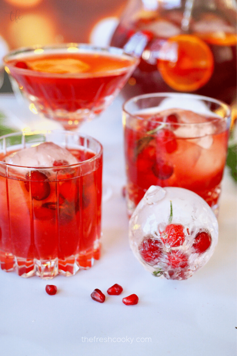 Pomegranate Punch poured into three different crystal cocktail glasses with a decorative ice ball with frozen cranberries inside.