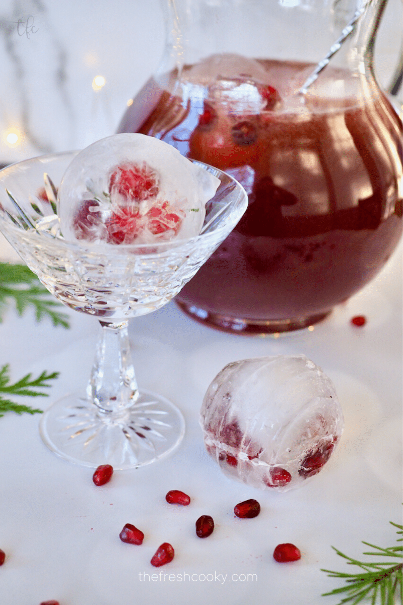 Pomegranate punch in a pitcher with a pretty cocktail glass filled with a Christmasy ice cube mold.