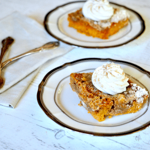 Pumpkin Pie Dump Cake sliced and on two plates, topped with swirls of whipped cream.