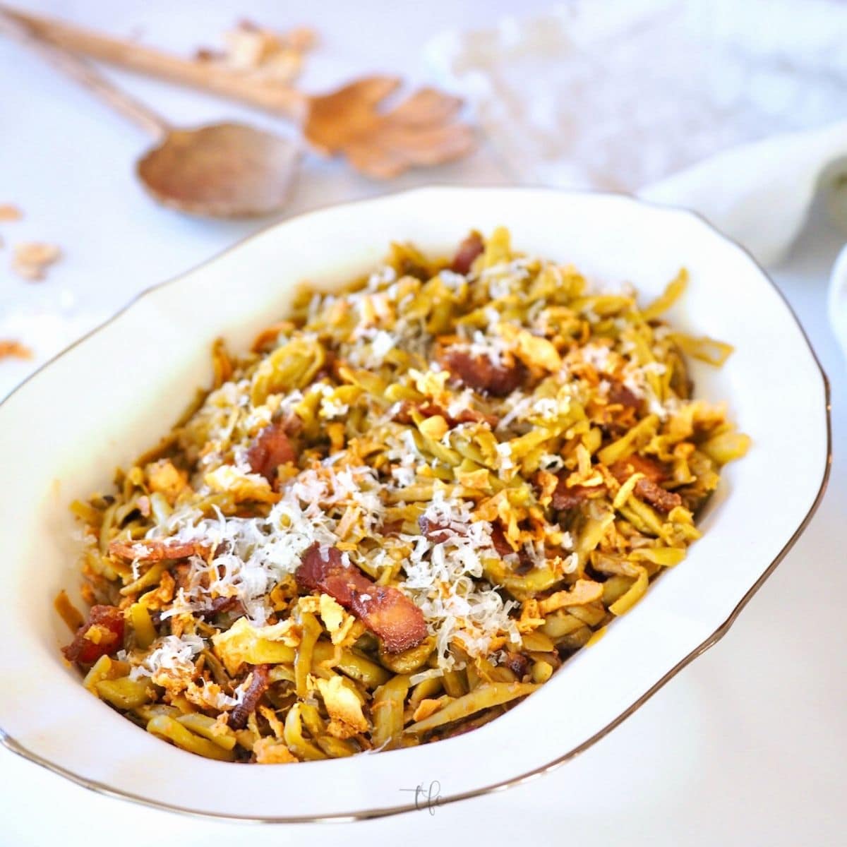 Canned Green Beans recipe with bacon, top down shot with recipe in pretty bowl and spoons in the background.