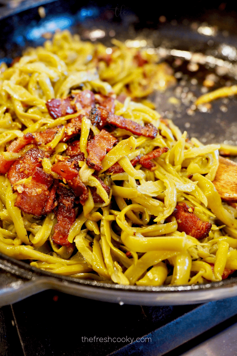 Spoonful of green beans with bacon in skillet. 