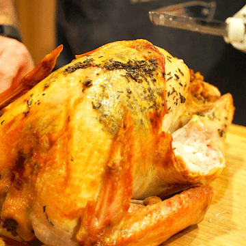 Roasted turkey on cutting board with man carving the turkey.