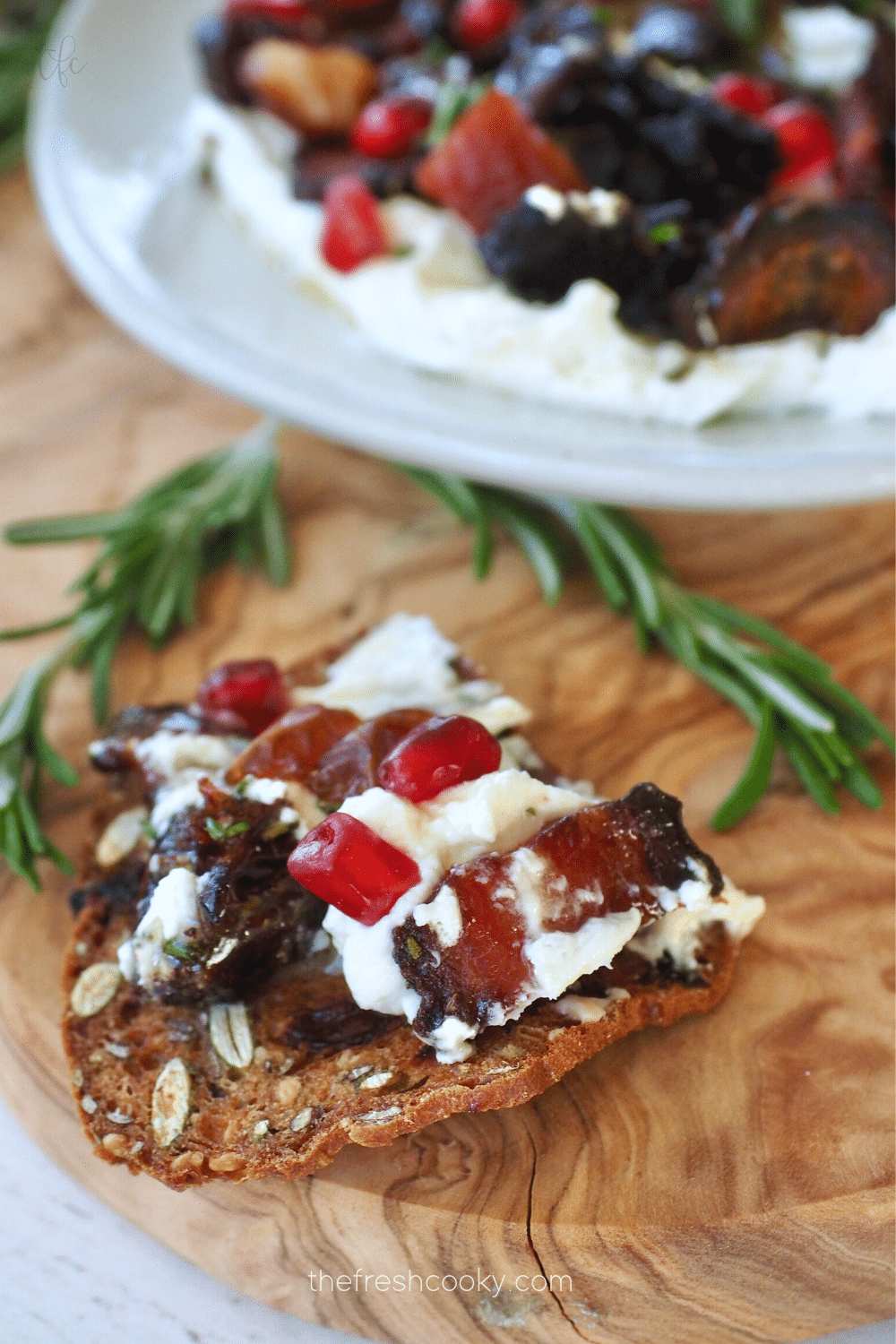 Whipped Goat Cheese Dip spread onto cracker with bacon and dates and pomegranates on top.