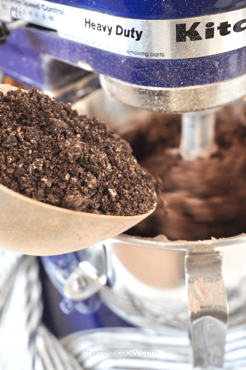 Pouring in crushed Oreo cookies into Oreo Crumbl Cookie dough batter. 