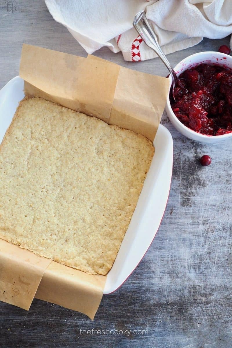 Baked shortbread crust with cranberry puree nearby for lemon cranberry bars. 