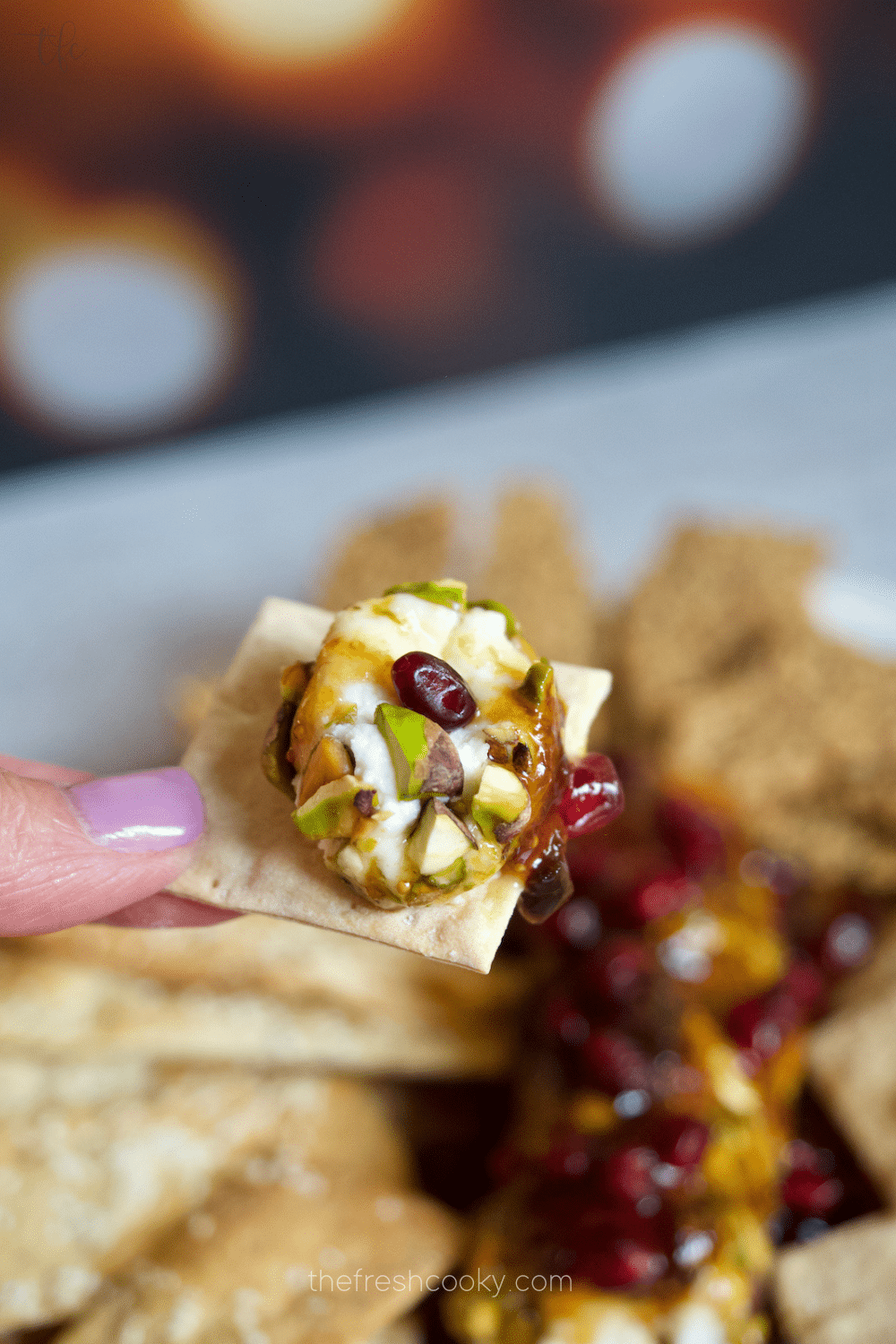 Goat cheese crusted in pistachios and drizzled with fig and hot honey on a cracker with hand holding.