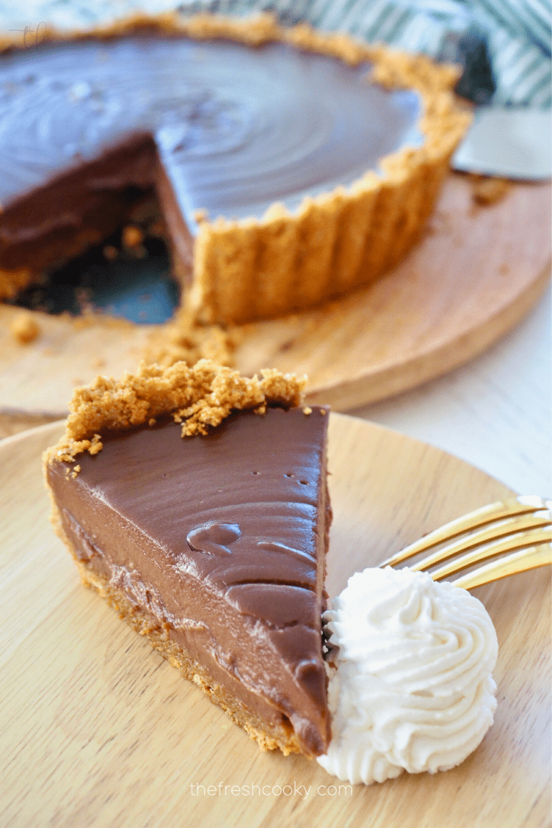 Sliced no bake chocolate pie with graham cracker crust and dollop of whipped cream on plate with pie in background.