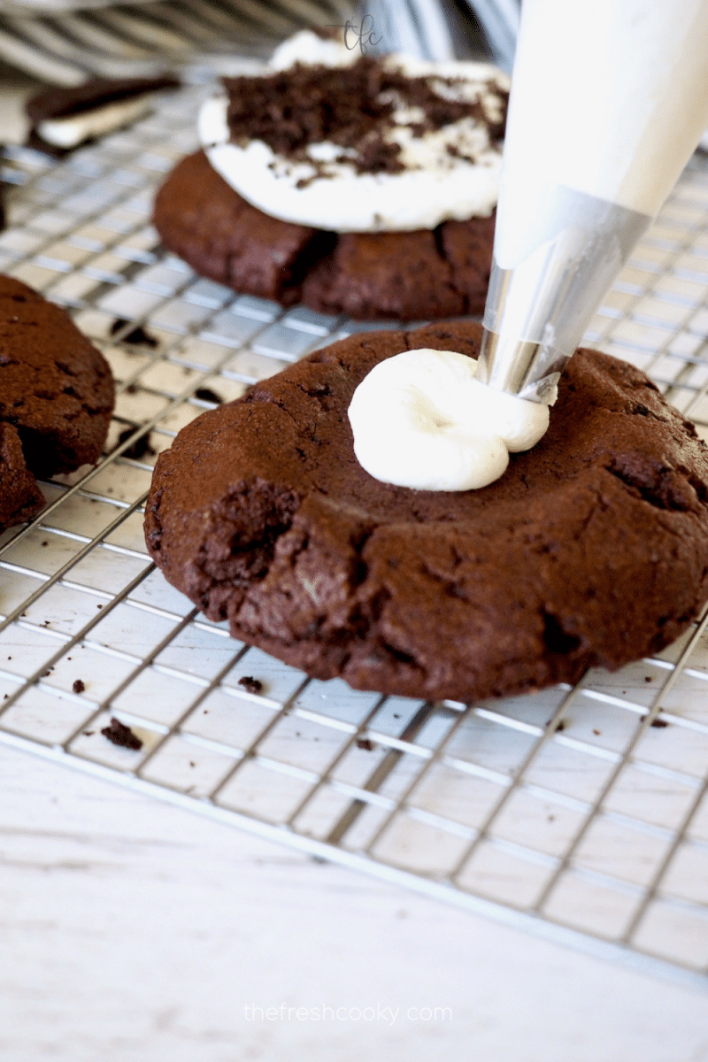 Piping on vanilla buttercream onto Oreo Crumbl Cookie.