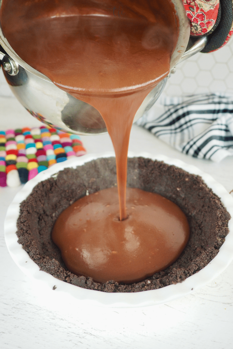 Pouring hot chocolate pudding mixture into oreo cookie crust pie shell.
