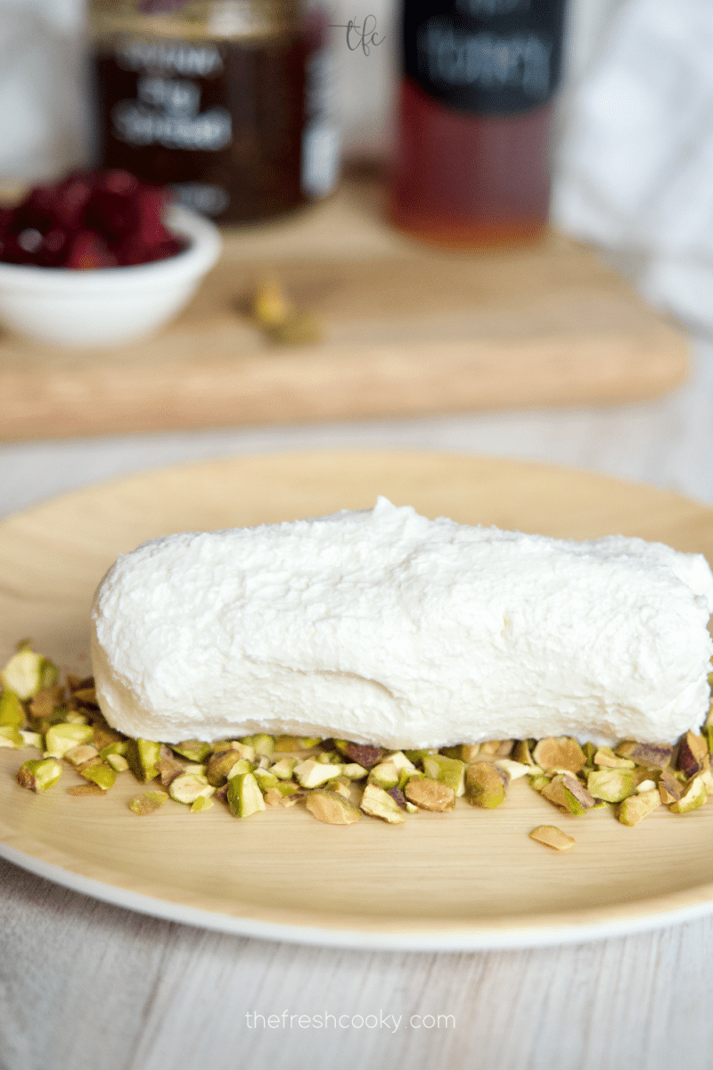 Goat cheese log being rolled in crushed pistachios. 