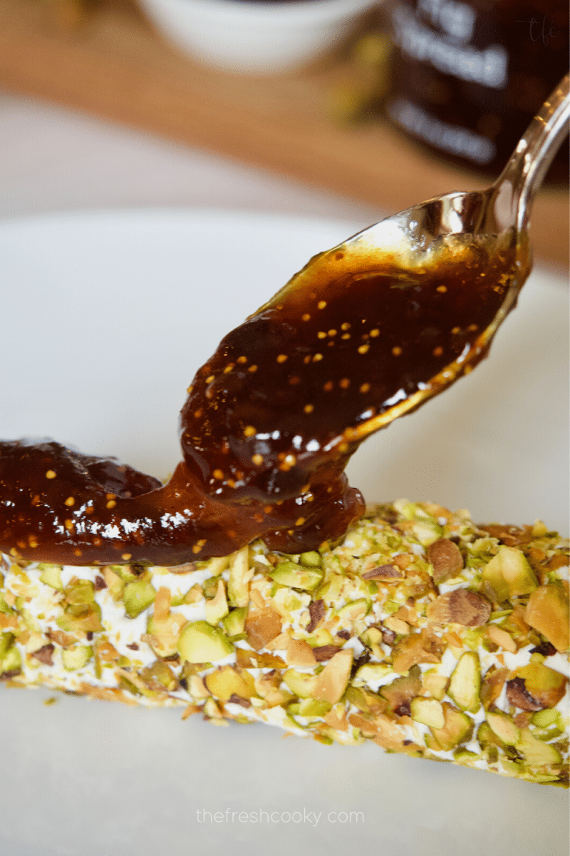 Spooning fig preserves over pistachio-crusted goat cheese log. 