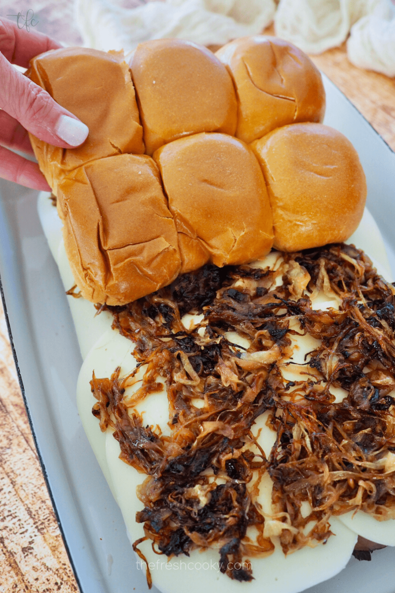 Adding tops of rolls to layered roast beef slider sandwiches. 