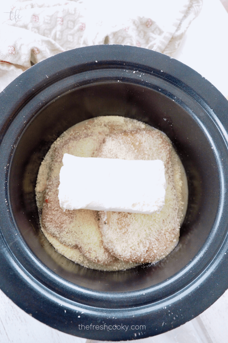 Adding block of cream cheese to the top of the chicken for Olive Garden Crock Pot Chicken.