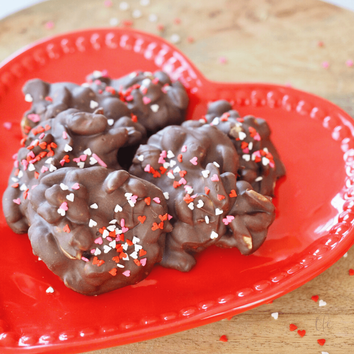 Crockpot Peanut Clusters on red heart plate with heart sprinkles.