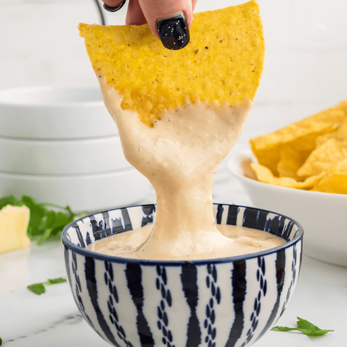 Hand dipping tortilla chip into queso cheese dip.