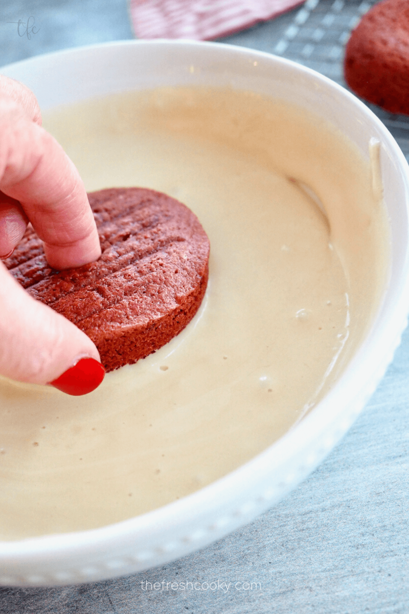 Dipping red velvet donut into glaze. 