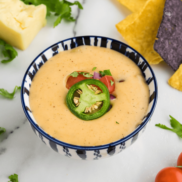 Queso cheese dip in blue and white bowl garnished with jalapeños and tomatoes.
