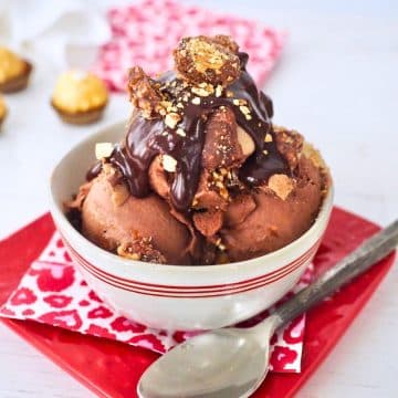 Three scoops of Ferrero Rocher Ice Cream in a bowl, topped with hot fudge and broken Ferrero Rocher Candies.