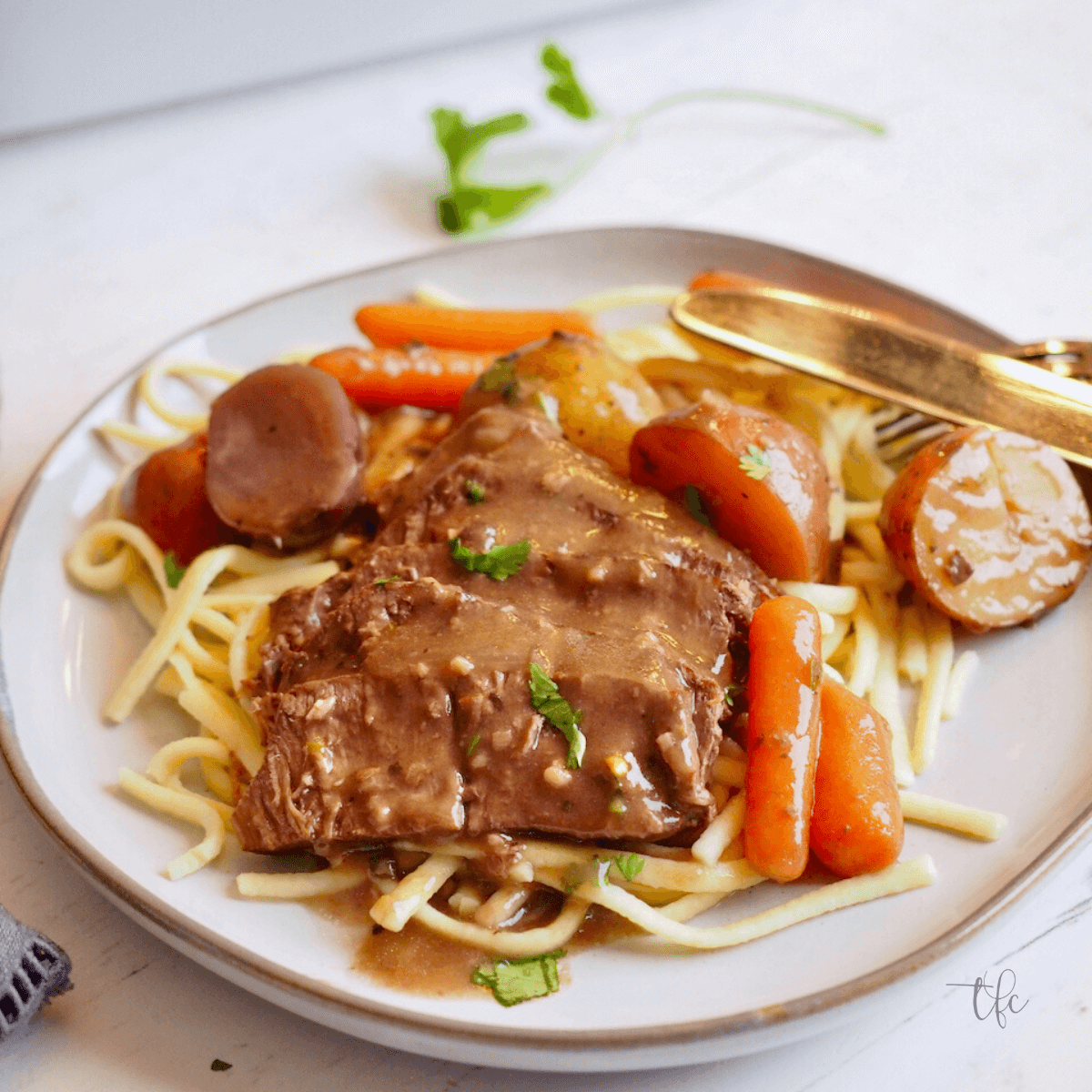 Crockpot London Broil Recipe sliced london broil on a plate of egg noodles smothered in rich gravy with carrots and potatoes.