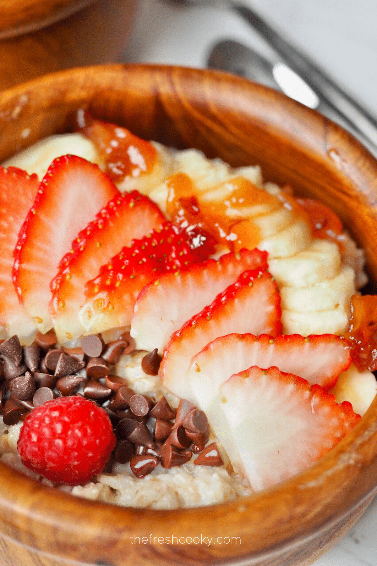 Old Fashioned Rolled Oats made in the instant pot, in a wooden bowl with sliced bananas, strawberries and mini chocolate chips.