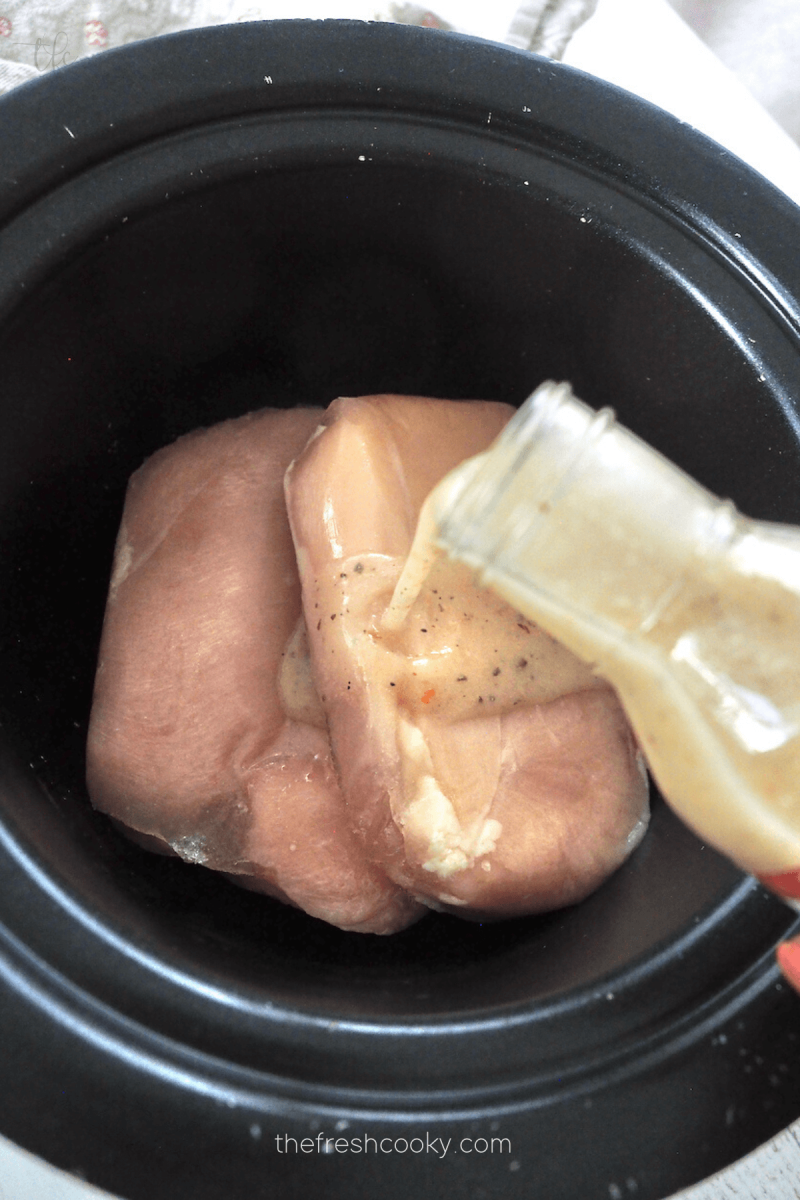 Pouring bottle of Italian Dressing over chicken (fresh or frozen) for Olive Garden Crock Pot Chicken. 