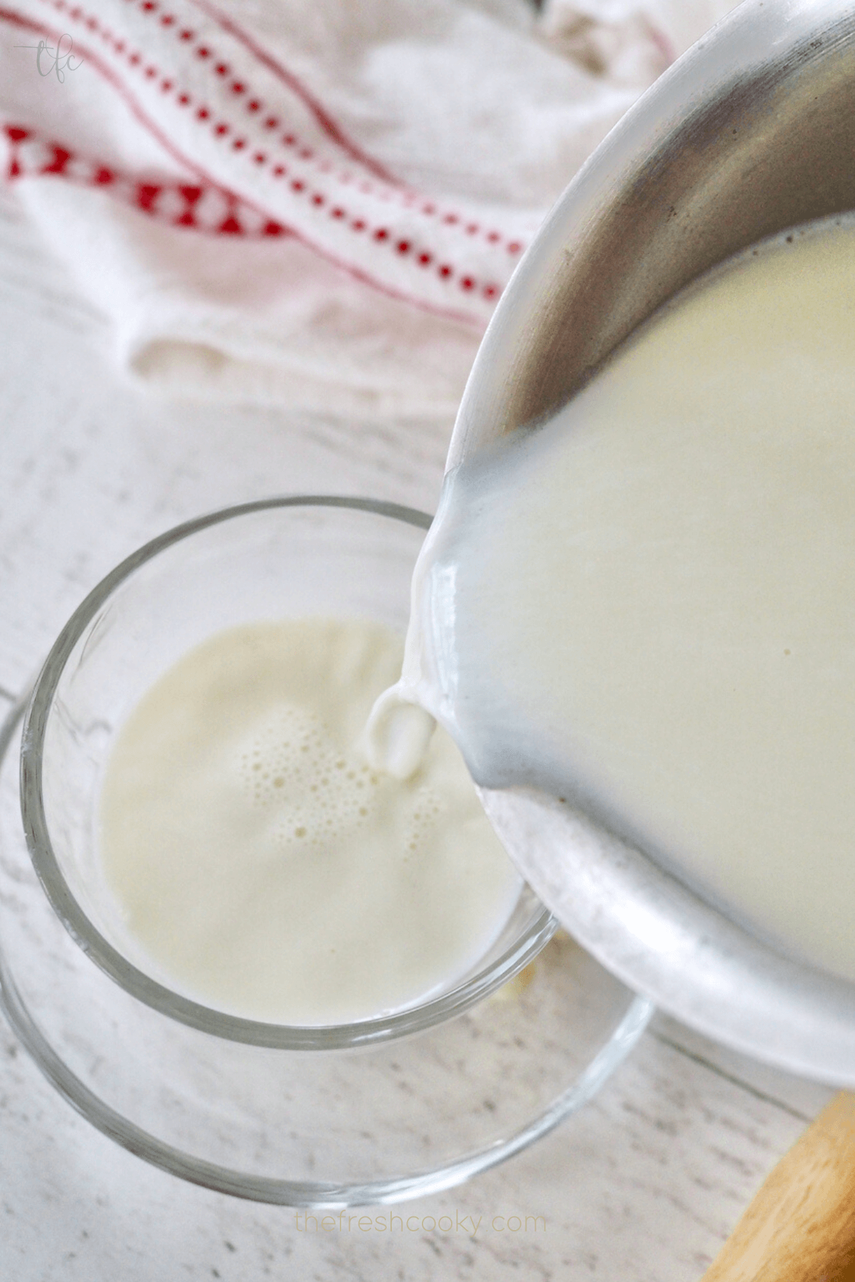 Pouring white hot chocolate into a glass mug.