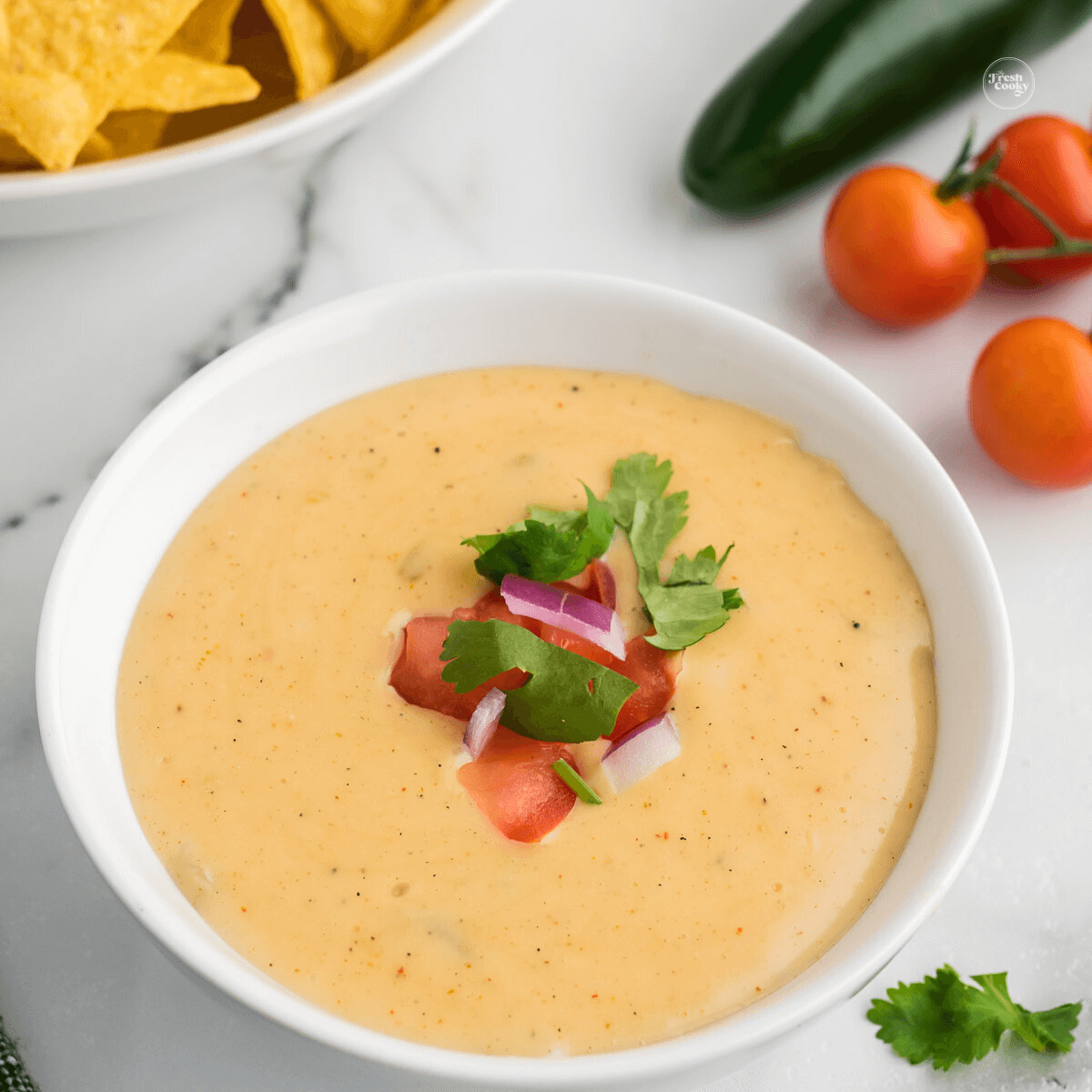 Creamy white queso dip in white bowl topped with fresh veggies.