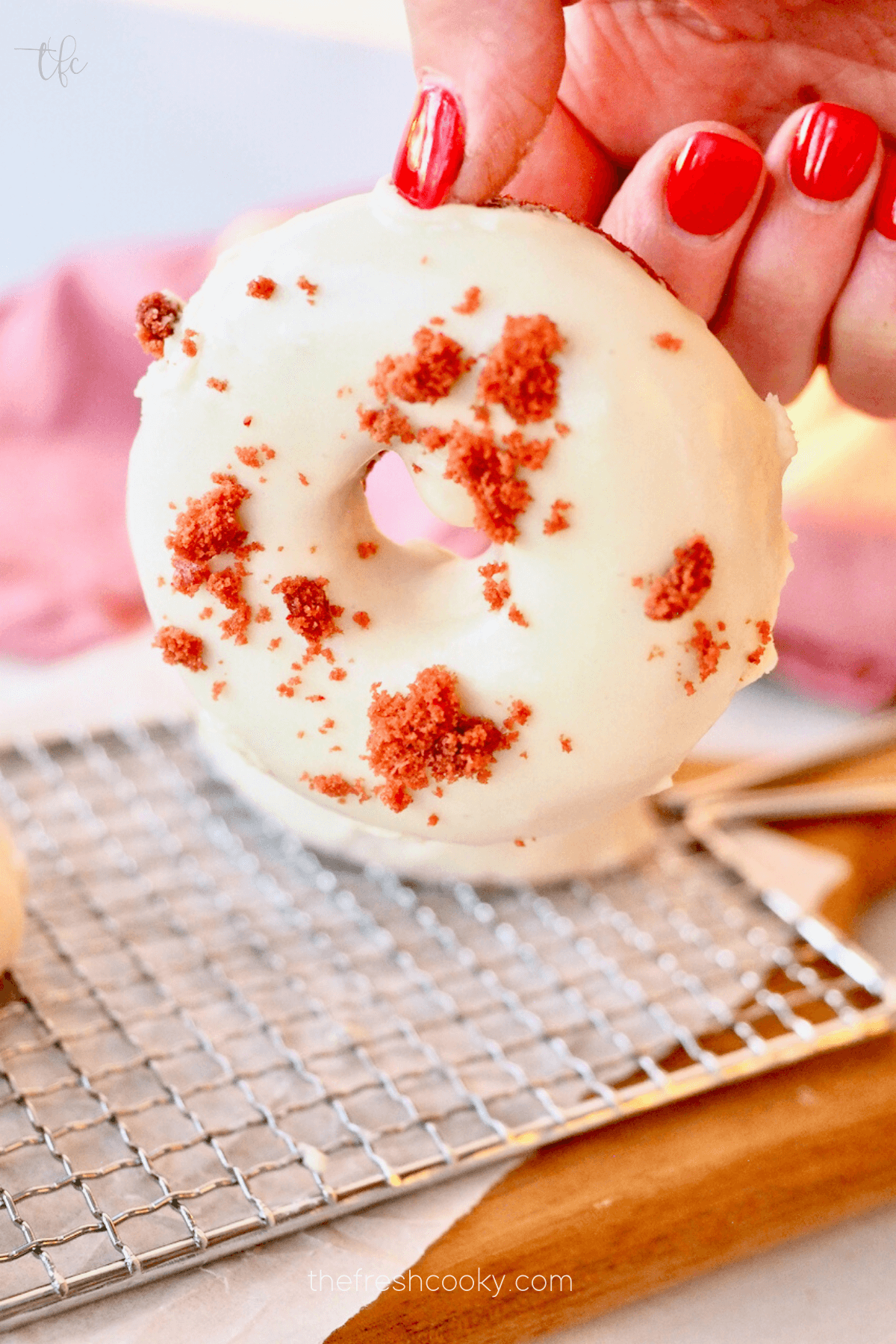 Red Velvet Donut being held in hand with delicious cream cheese glaze.