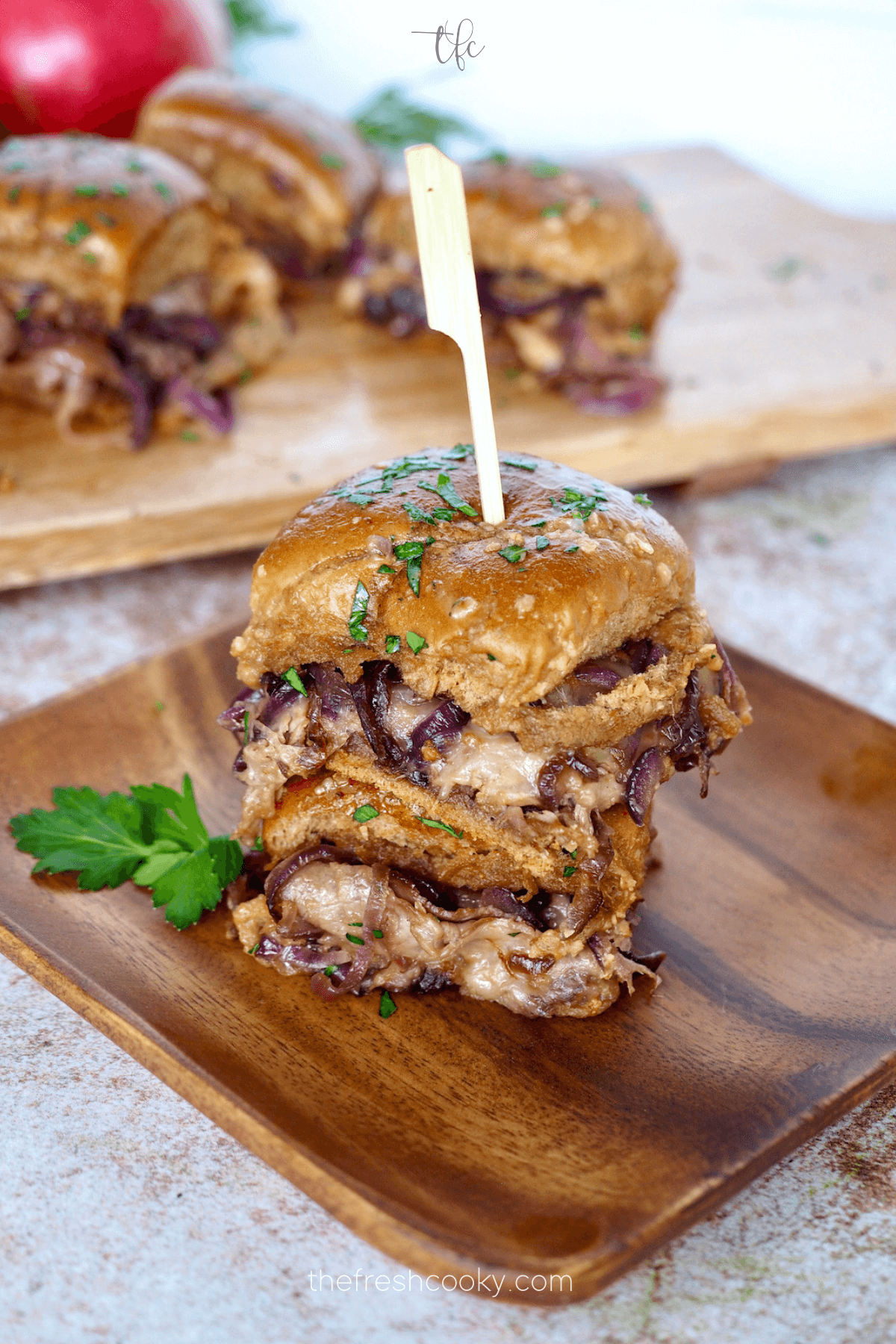 Roast beef sliders stacked with a pick and on a wooden plate.