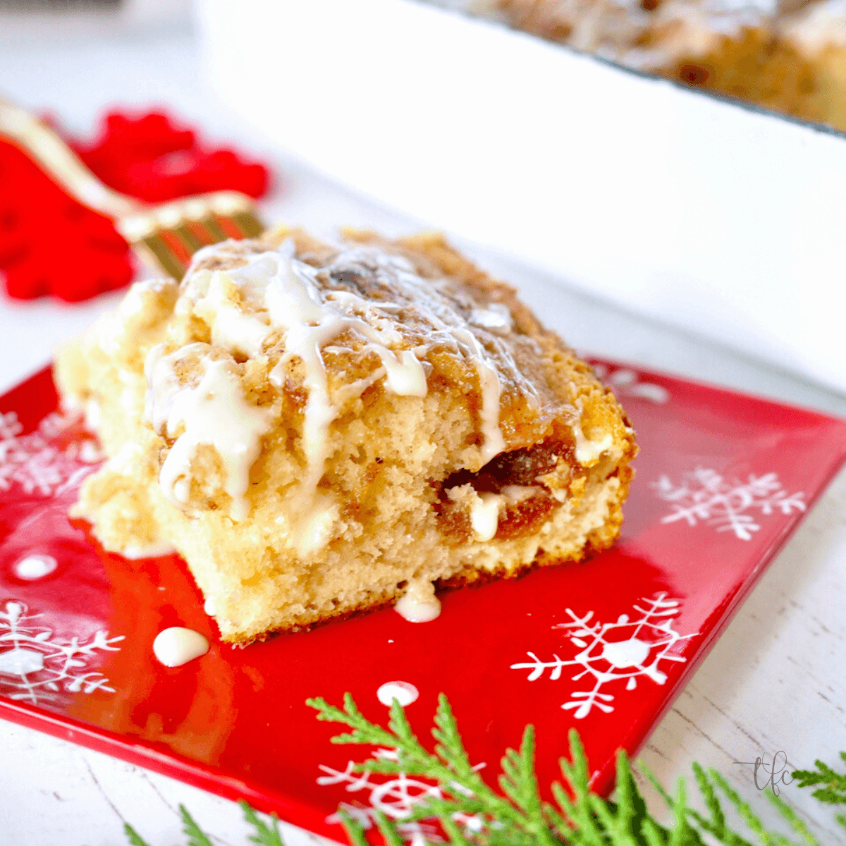 Slice of eggnog coffee cake on a pretty red winter plate with greens.