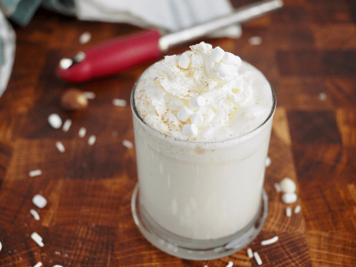 Steaming Starbucks white hot chocolate in glass mug with nutmeg, whipped cream and mini marshmallows.