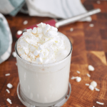 Starbucks White Hot Chocolate in a glass mug topped with whipped cream, jimmies, mini marshmallows and nutmeg.