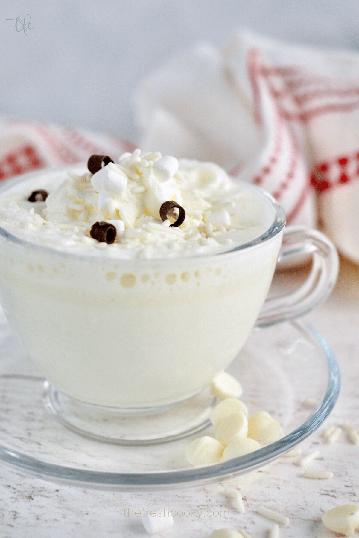 Starbucks White Hot Chocolate Copycat recipe in glass cup with plate and garnished with whipped cream and sprinkles.