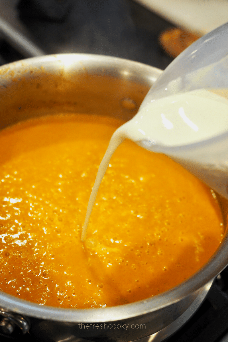 Pouring in half and half and heavy cream into mixture for creamy tomato bisque recipe. 