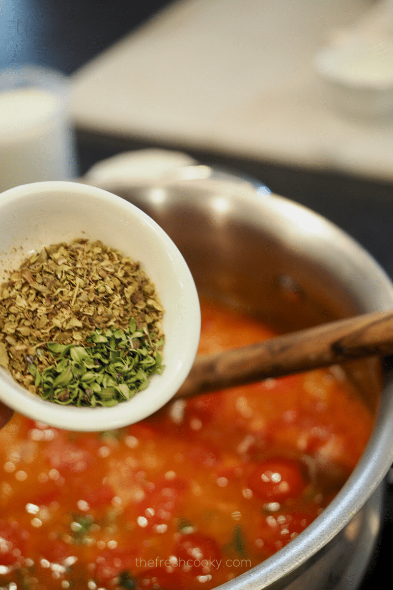 Adding herbs and salt and pepper creamy tomato bisque recipe.