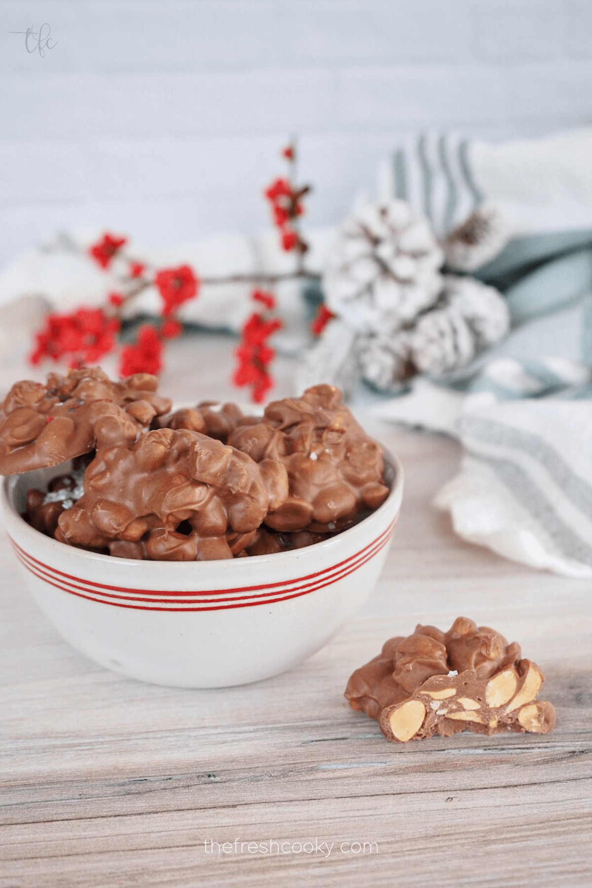 Bowl filled with chocolate peanut clusters with one on table with bite taken out.