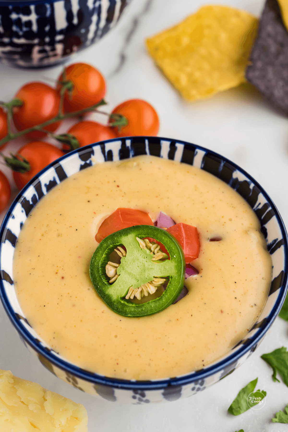 Queso cheese dip in pretty bowl garnished with jalapeno, tomato, cilantro and diced onions.