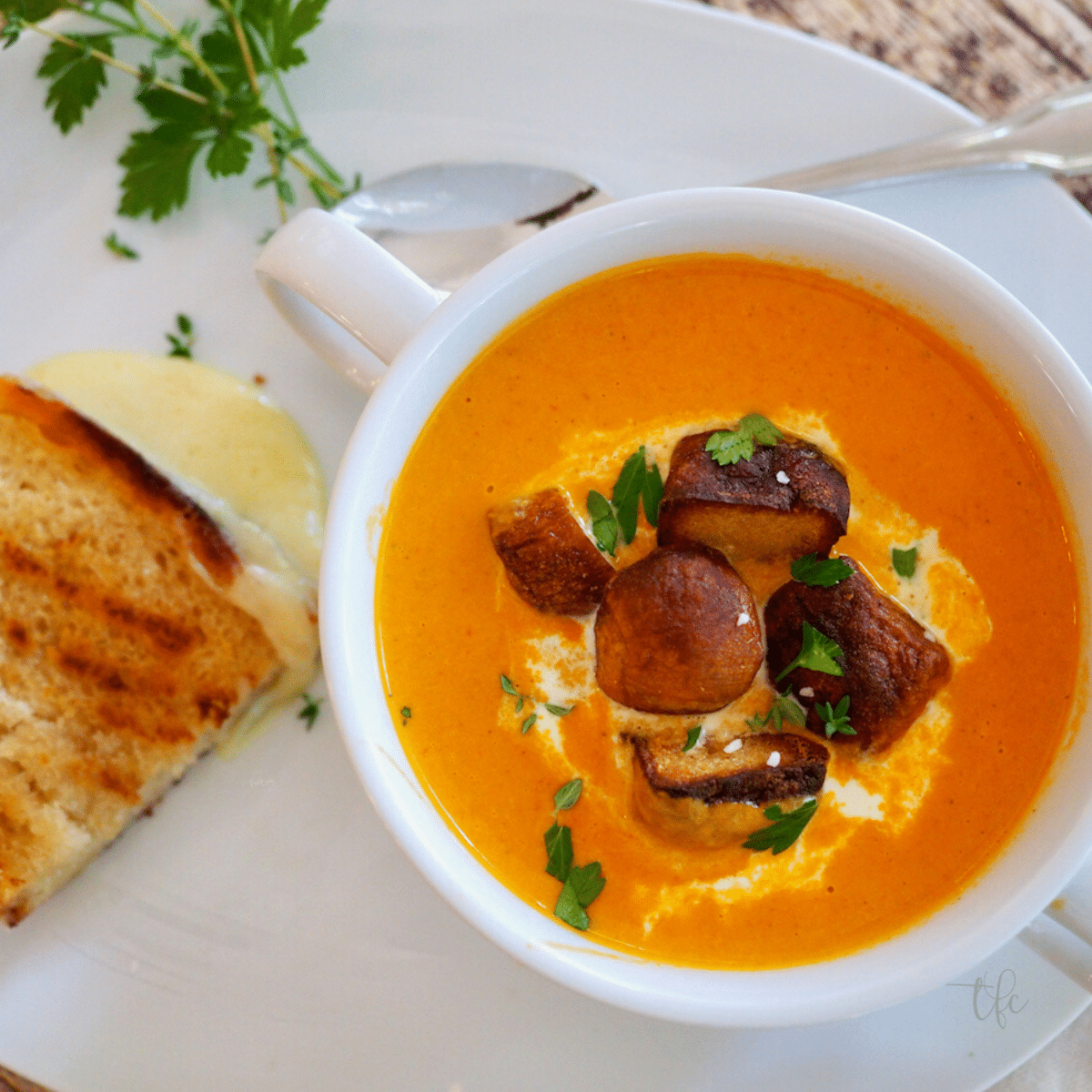 Creamy tomato bisque recipe square top down shot of soup with croutons in white bowl with grilled cheese.