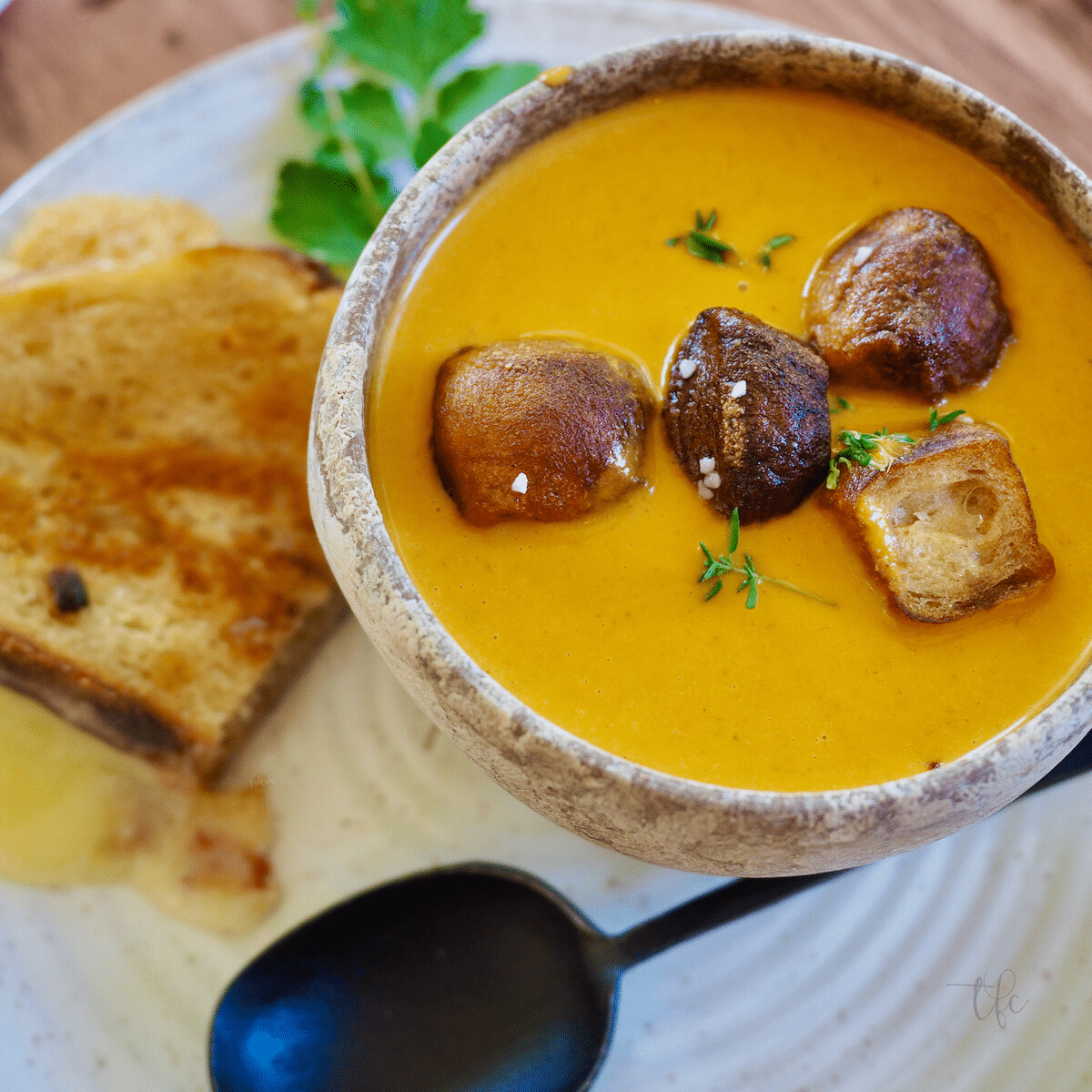 Creamy tomato bisque recipe top down shot with rustic bowl filled with silky tomato soup, topped with croutons and a grilled cheese sandwich on the side.