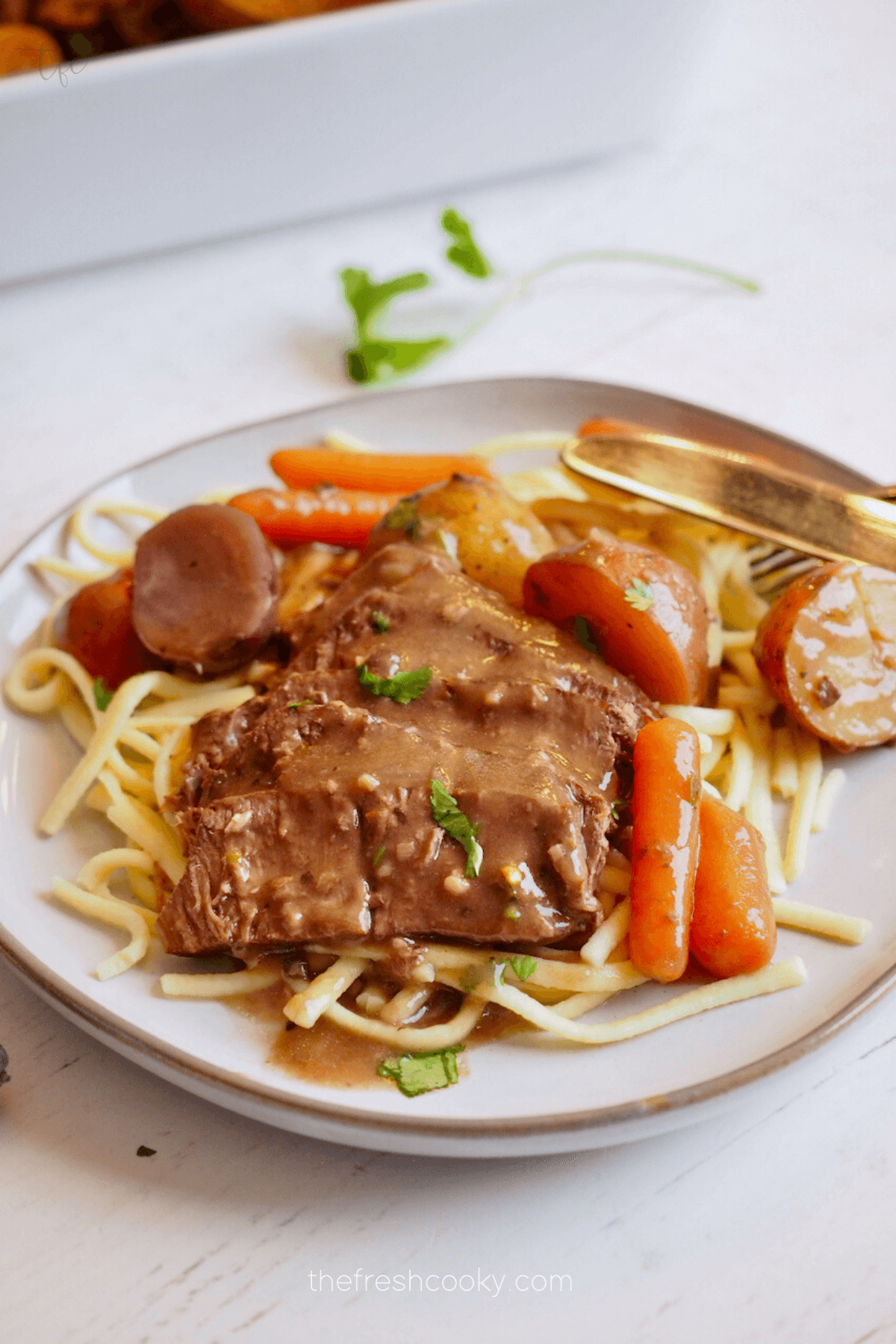 Crockpot London Broil on a plate with egg noodles, carrots and potatoes.