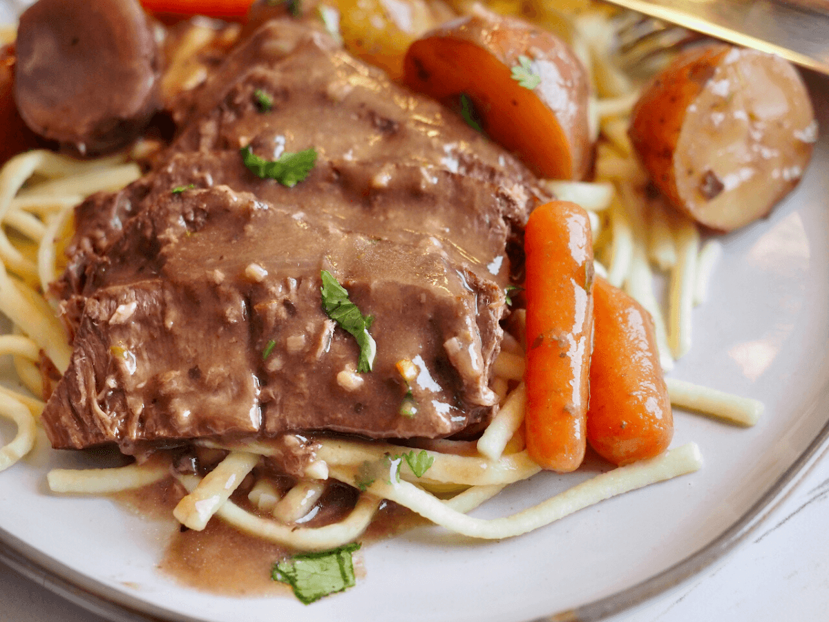 Crockpot London Broil close up with gravy on egg noodles.