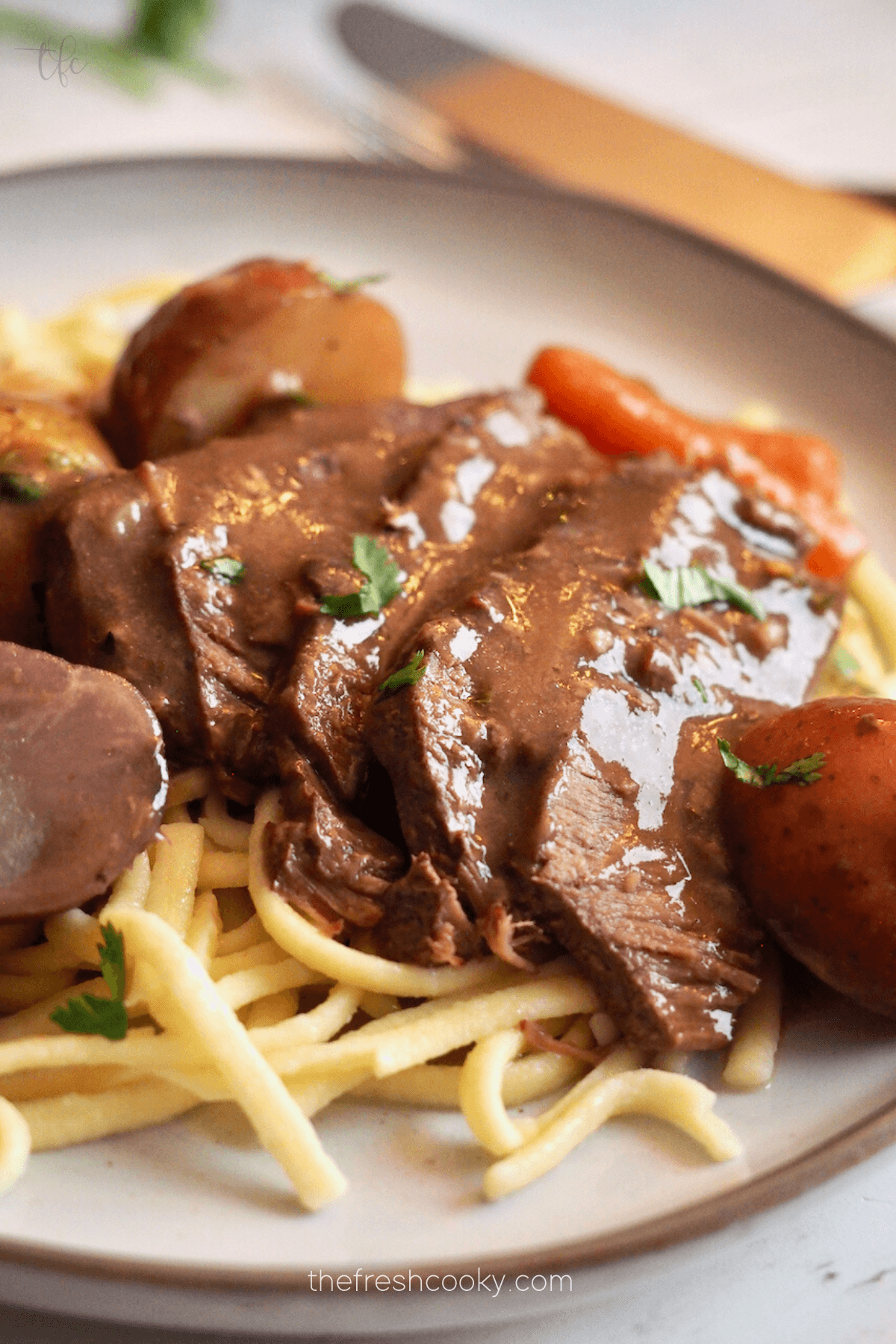 Crockpot London Broil recipe over egg noodles, on a plate with veggies and gravy.