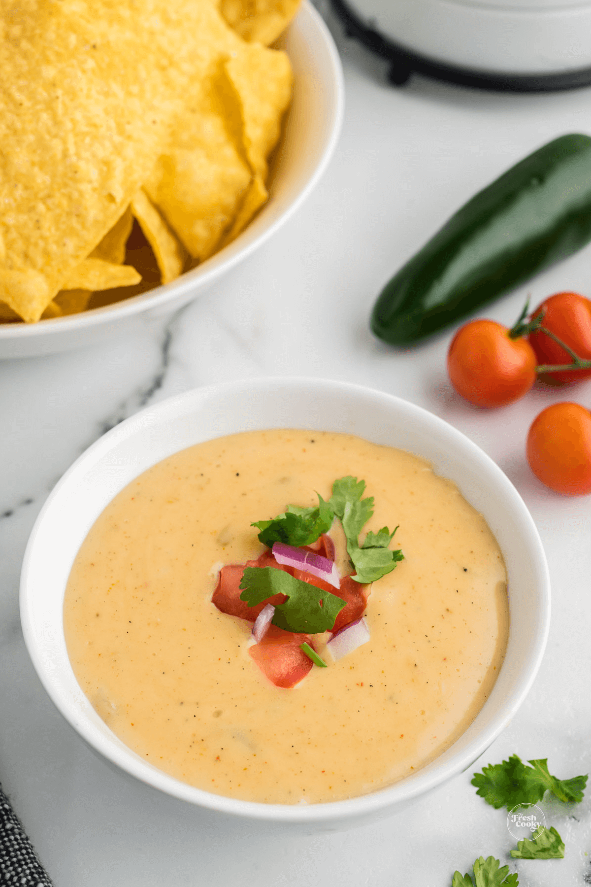 Bowl of creamy all natural queso dip with tortilla chips and garnish.