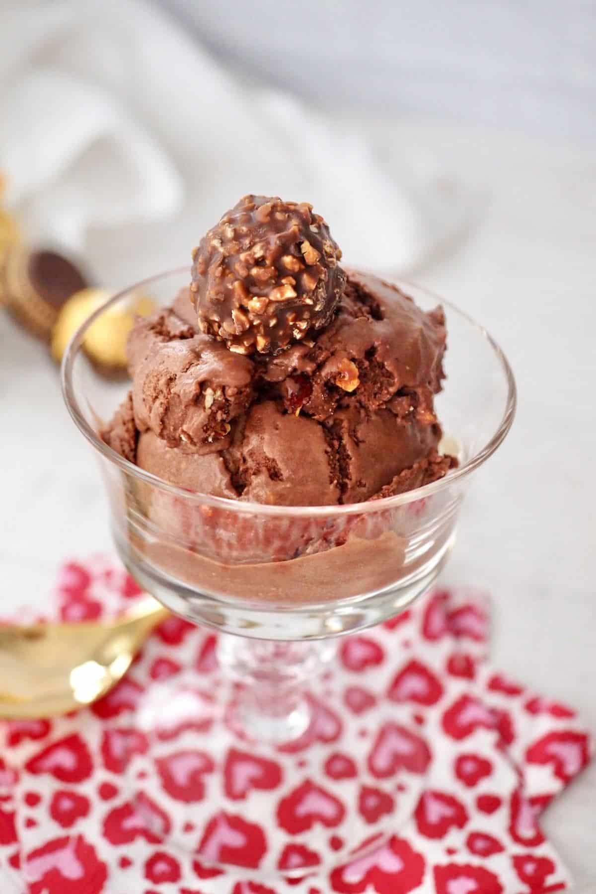 Two scoops of ferrero rocher ice cream in coupe gass topped with a Ferrero Rocher chocolate.