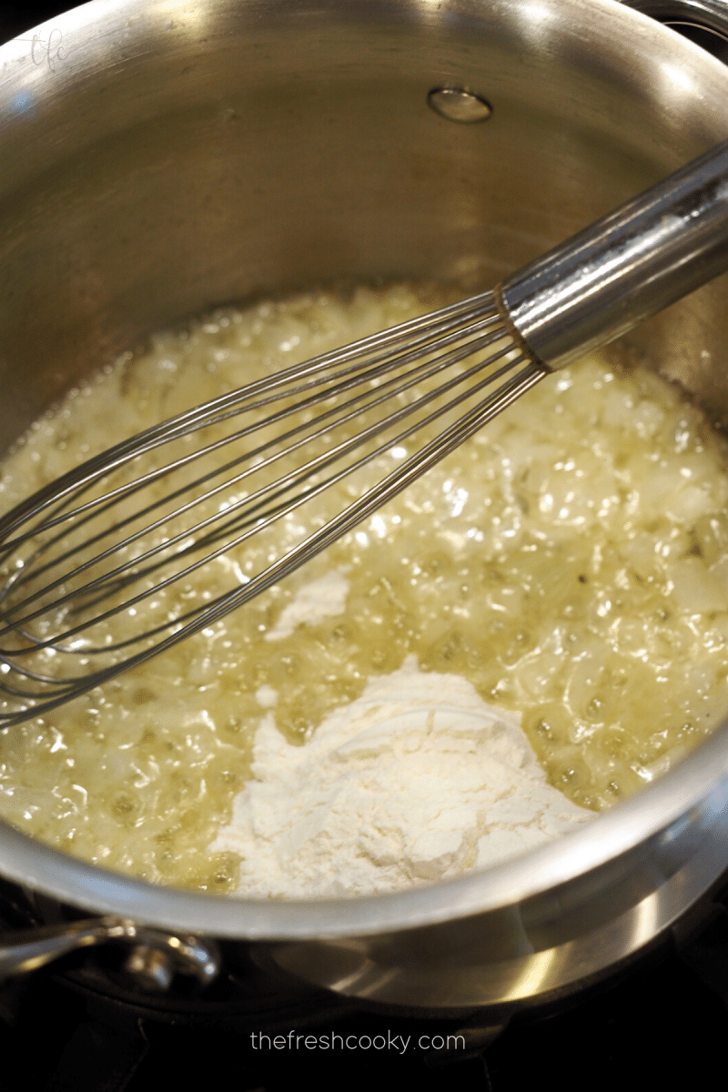 Adding flour to saucepan with caramelized onions for creamy tomato bisque recipe. 